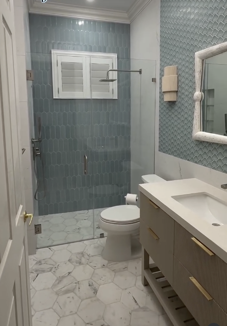 Coastal bathroom with blue picket tile, a glass shower and marble hexagon floor