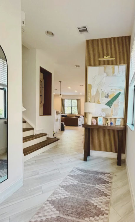Bright entryway with a wood-slat accent wall, console and layered art opening to the great room