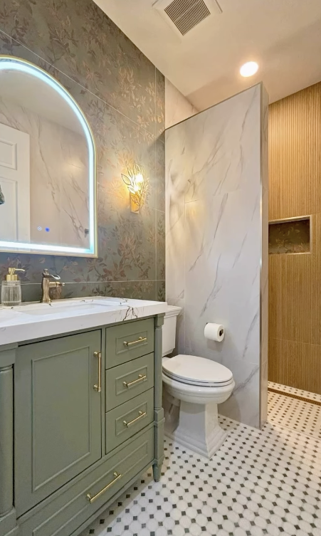 Bathroom after full renovation — sage-green vanity, backlit arched mirror and marble tile