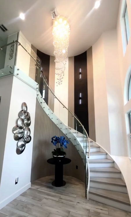 Grand curved staircase with a cascading crystal chandelier and glass railing